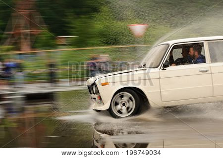Orel Russia July 22 2017: Dynamica car festival. White tuned Russian car VAZ Lada rides at full speed on puddles and splashes water with reflections and motion blur