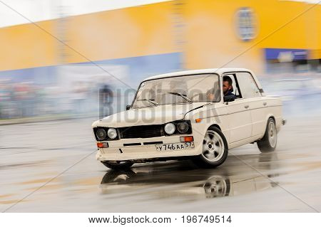 Orel Russia July 22 2017: Dynamica car festival. White tuned Russian car VAZ Lada swiftly drift rides on wet asphalt with industrial background motion brur