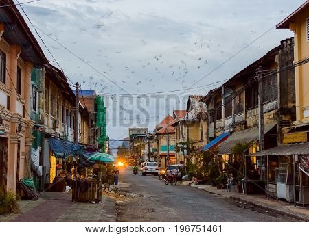 Evening in the city. Many birds fly fast in the sky at sunset. Street of Kampot Old Town. Cambodia