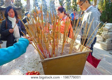 HONG KONG, CHINA - JANUARY 22, 2017: Close up of incenses burning up, with people behind of Wong Tai Sin Buddhist Temple to pray, in Hong Kong, China.