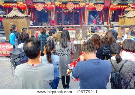 HONG KONG, CHINA - JANUARY 22, 2017: Crowd of people holding a their hands an incense sticks and praying inside of Wong Tai Sin Buddhist Temple to pray, in Hong Kong, China.