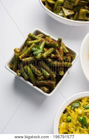 A Masala or fried vegetable dish consisting of green beans, onions, and curry spices, served in square bowl, selective focus