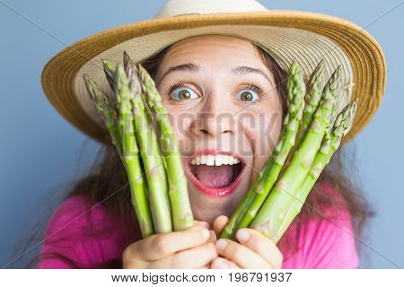 Close-up portrait of funny surprised woman is holding asparagus in front of her face.