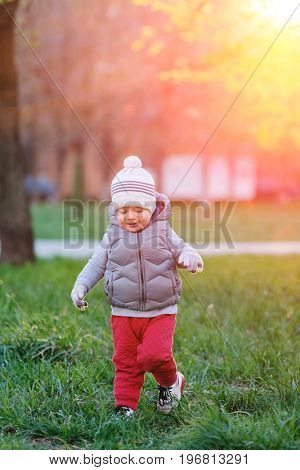 Portrait of toddler child in warm vest jacket outdoors. One year old baby boy wearing vest jacket at park meadow during sunset. 