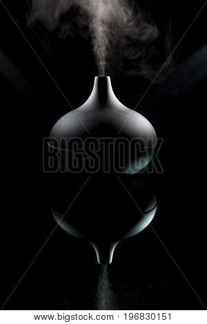 Complimentary therapy and alternative medicine. Modern aromatherapy aroma diffuser working. Dark moody image backlit with spotlights against black background. Modern design image also reflecting questions on whether alternative medicine has a sinister sid
