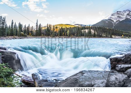 The full-water bubbling waterfall of Athabasca. Cold blue water at sunset. Clear autumn evening in Canada. The concept of extreme and ecological tourism