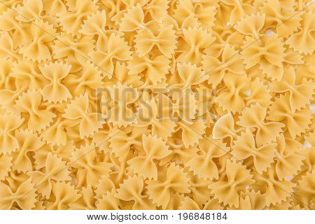 Uncooked bow-tie or farfalle pasta. Tasty traditional farfalle Italian macaroni. High quality, delicious, hard, raw and bright yellow texture close-up. Flour products.