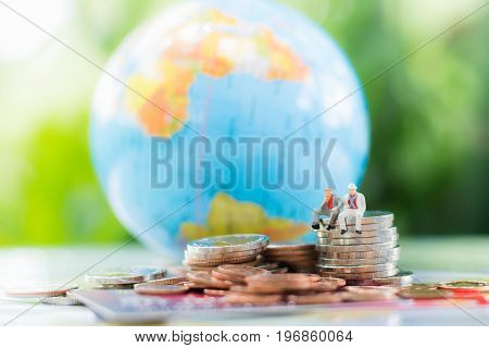 Miniature businessman sitting on the stack of coins with credit card or debit card blurred globe and a pile of coins background using as commitment agreement investment partnership E-commerce and online business concept.