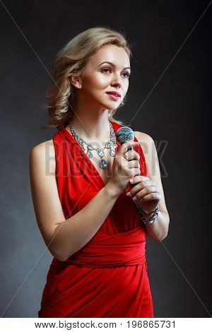 half length portrait of beautiful young woman in red dress holding microphone in her hand singing satanding next to color background