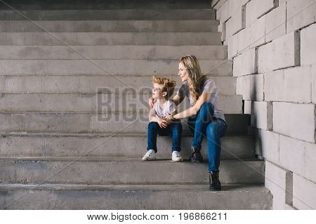 Mother with son sitting on a stairs and looking somewhere