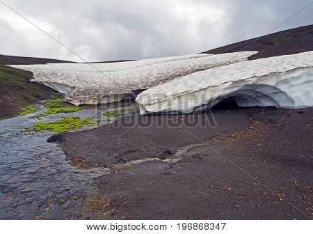 Iceland Snow Ice Cave And Stream In Sad Deserted Lnadscape With Bright Green Moss