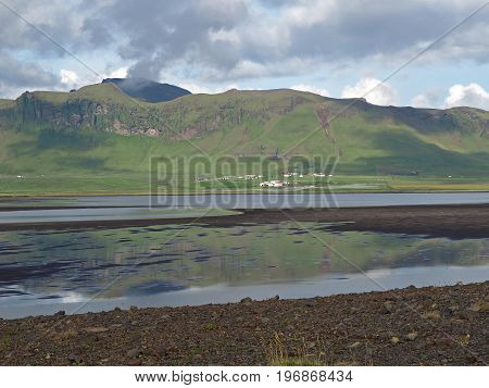 Iceland Green Hills Near Vik Village With Shallow Water Lake And Dark Clouds Reflected On Water