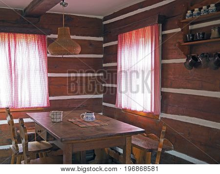 interior of old timbered cattage house with oak table chairs and painted cups with two windows with checked curtains