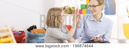 Young happy teacher congratulating good work to her little student
