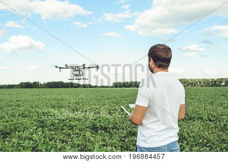 Young man operating of flying drone octocopter at the green field. Professional agriculture drone flying with blue sky.