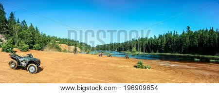 People driving ATV quads on sand beach at lake. Panoramic view. Ontario. Canada.