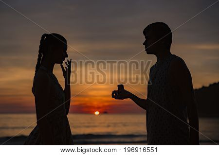 A silhouette man propose marriage to a silhouette woman with sunrise background