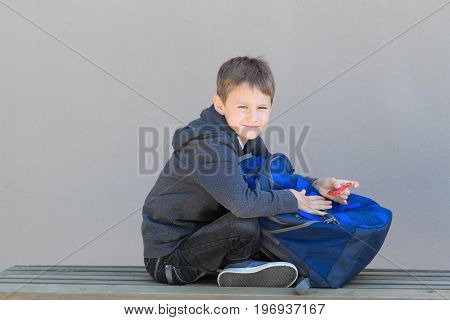 Boy with backpack and spinner sitting on the bench after school