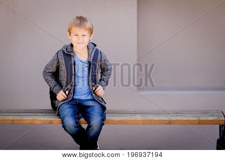 Child with backpack sitting on the bench near the school