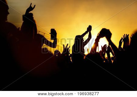 Young girl enjoys a rock concert, Silhouette on sunset, hands up on openair