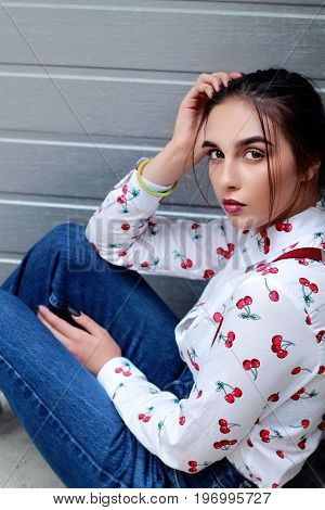Closeup Fashion Portrait Of Young Pretty Hipster Girl Siting On Ground With Dark Brown Hairs Wearing