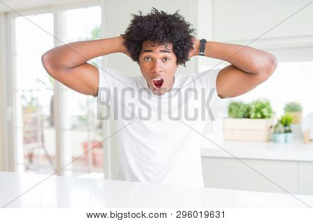 Young african american man wearing casual white t-shirt sitting at home Crazy and scared with hands on head, afraid and surprised of shock with open mouth