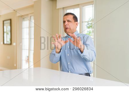 Middle age man sitting at home afraid and terrified with fear expression stop gesture with hands, shouting in shock. Panic concept.
