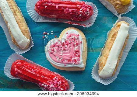Eclairs With Vanila, Raspberry And Mango Flavors And Pink Heart Shaped Cookie On Blue Wooden Backgro