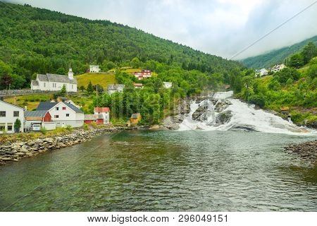 Houses On Mountainside By Lake Near The Waterfall. Mountain River Flows Into Lake From Top Of Mounta