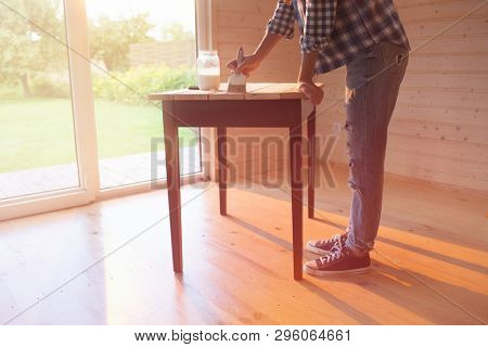 Woman with brush painting with varnish wooden center piece of a vinage renovated table. Hobby and house work concept