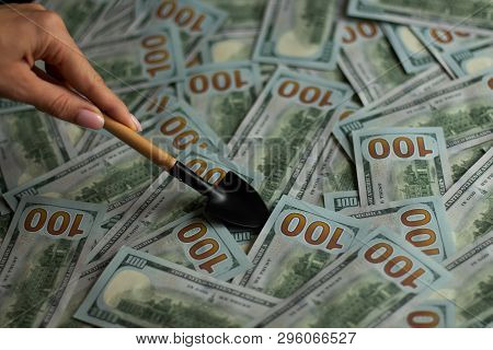 A Lot Of Bills In 100 Dollars And A Hand With A Small Shovel