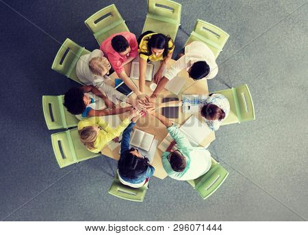 education, school, teamwork and people concept - group of international students with books and tablet pc computers putting hands on top of each other sitting at table