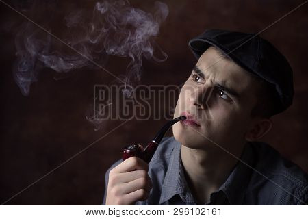 Closeup Portrait Of Young Man With Beret Hat, Smoking A Tobacco Pipe. Thinking About Something. Huma