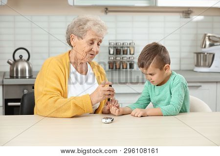 Senior Woman With Her Grandson Using Lancet Pen At Home. Diabetes Control