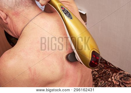 An Old Man With Gray Hair Doing His Own Neck Massage With An Electric Massager At Home. Restoration 