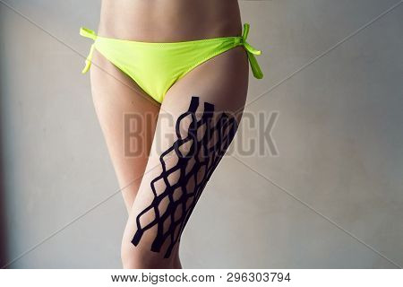 Kinesiotaping The Legs Of The Girl Standing In Front Of A White Wall In The Studio