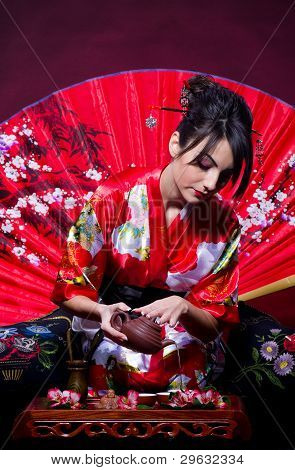 Woman in red Asian costume arranging Japanese tea ceremony