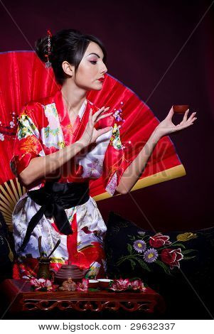 Woman in red Asian costume arranging Japanese tea ceremony