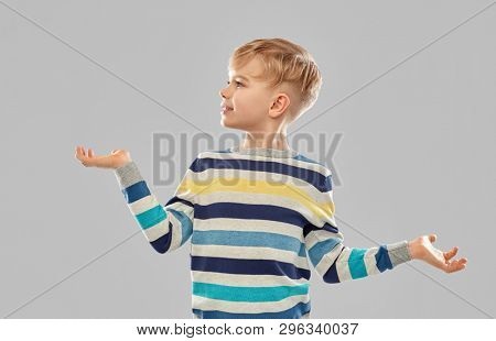 childhood, gesture and people concept - portrait of smiling little boy in striped pullover holding something imaginary on empty hands over grey background
