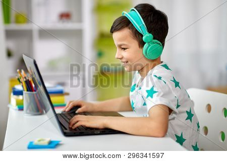 technology, gaming and people concept - boy in headphones playing video game on laptop computer at home