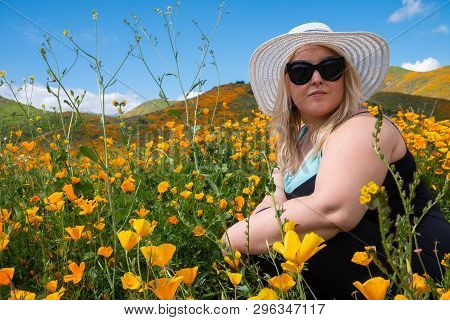 Blonde Woman Wearing A Straw Bonnet Hat Looks Out To The Field Of Poppy Wildflowers During The Super