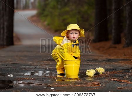 A small child plays in the rain while little chicks try to get a drink of water