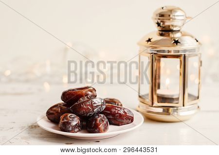 Dried Dates On White Plate And Lantern With Burning Candle On White Wooden Table, Bokeh Light On Bac