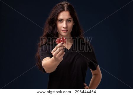 Curly Hair Brunette Is Posing With Red Gambling Chips In Her Hands. Poker Concept On A Black Backgro