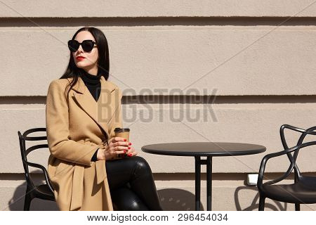 Charming Stylish Model With Red Lipstick Wearing Big Trendy Sunglasses, Beige Coat, Black Sweater An