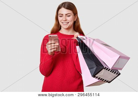 Young Beautiful Fashionable Caucasian Woman Holds Shopping Bags In One Hand And Smartphone In Anothe