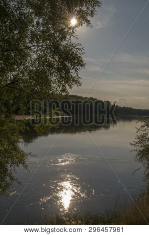 Wide River Flowing Across Green Forest. Fall. Evening. Reflections Of Sun In The Water
