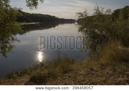 Wide River Flowing Across Green Forest. Fall. Evening. Reflections Of Sun In The Water