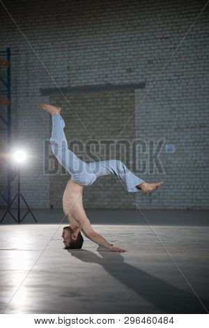 An Athletic Man On Capoeira Training. Performing A Stand On The Head With Spine Bend