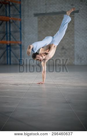 An Athletic Man On Capoeira Training. Standing On One Hand And Legs In The Split